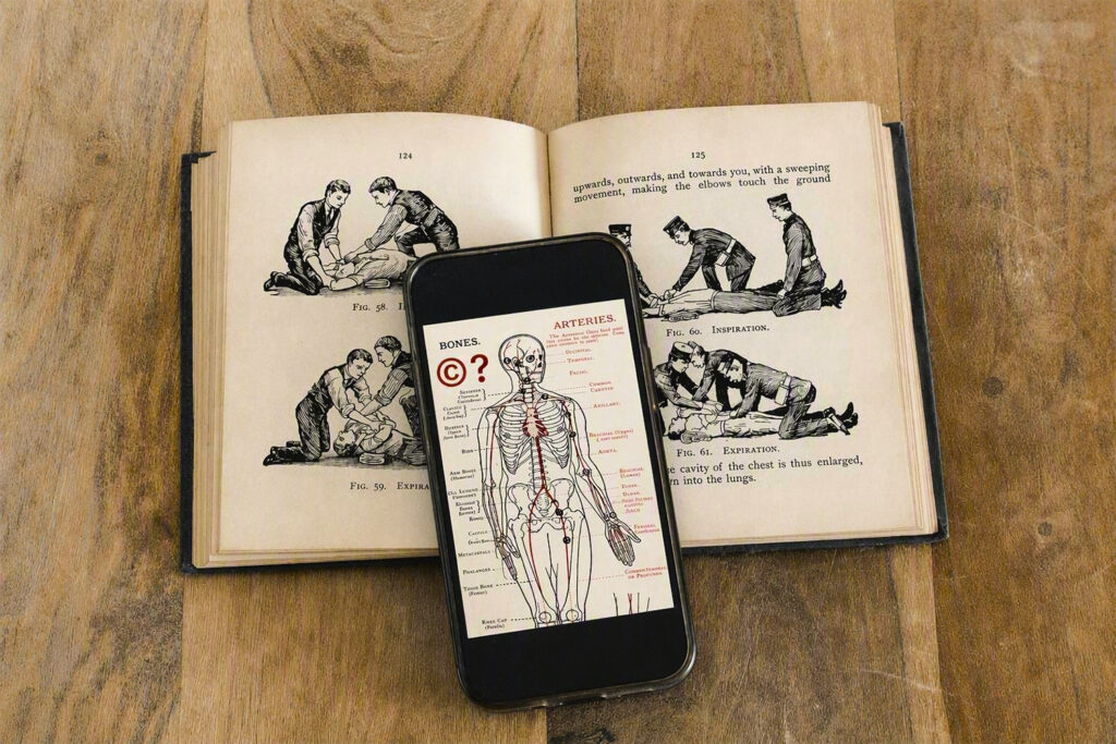 Image of a phone showing a drawing of a skeleton laying on top of an open book showing illustrations related to First Aid