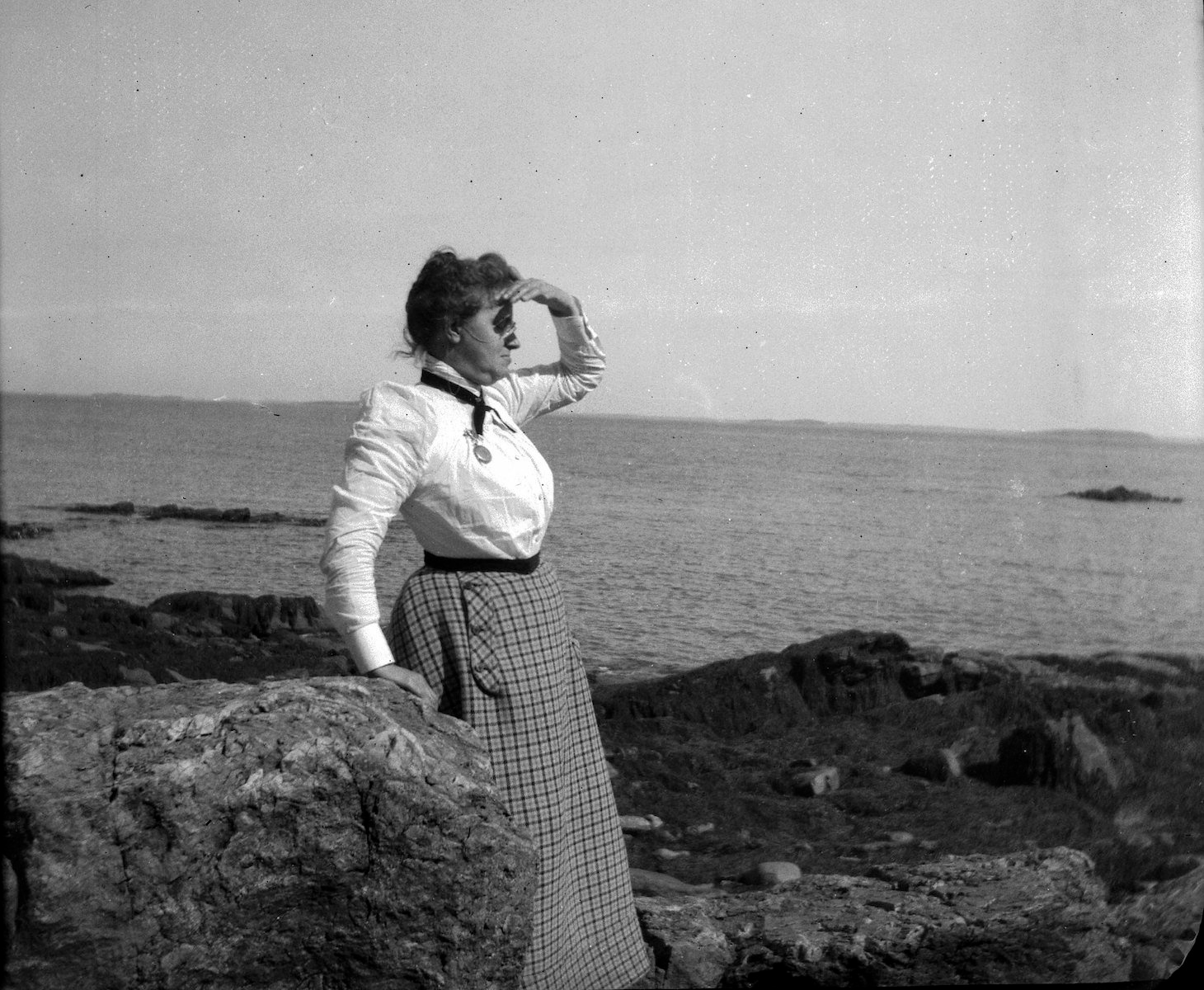strategy Black and white mage of a woman standing on a rocky coast looking out to sea, shading her eyes from the sun